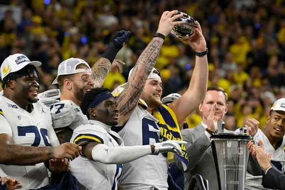 Kenneth Grant (78), Trevor Keegan (77), Mike Sainristil (0), Zak Zinter (65), Cornelius Johnson (6), and Big Ten Championship Trophy