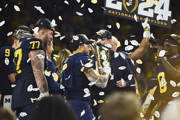 J.J. McCarthy (9), Trevor Keegan (77), Blake Corum (2), Jim Harbaugh, Mike Sainristil (0), and National Championship Trophy