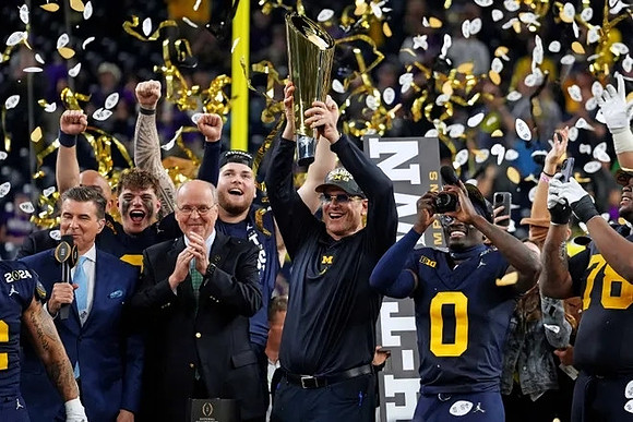 J.J. McCarthy (9), Zak Zinter (65), Jim Harbaugh, Mike Sainristil (0), Kenneth Grant (78), and National Championship Trophy