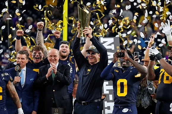 J.J. McCarthy (9), Zak Zinter (65), Jim Harbaugh, Mike Sainristil (0), Kenneth Grant (78), and National Championship Trophy
