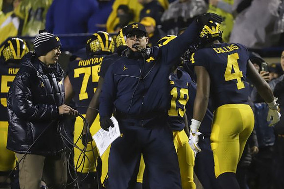 Cesar Ruiz (51), Jon Runyan Jr. (75), Jim Harbaugh, Mike Sainristil (19), and Nico Collins (4)