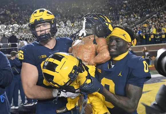 Luke Schoonmaker (86), Paul Bunyan Trophy, and Mike Sainristil (0)